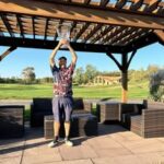 Man holding a trophy outdoors on a sunny day.