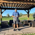 Man standing under a gazebo on a sunny day in a casual outfit.